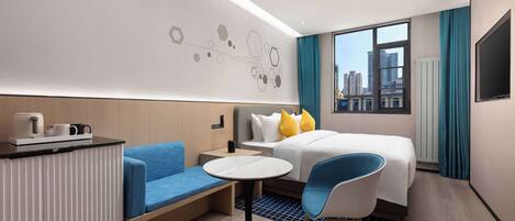 A modern hotel room with a bed, a desk with a chair, a small table, and a view of the city through large windows.