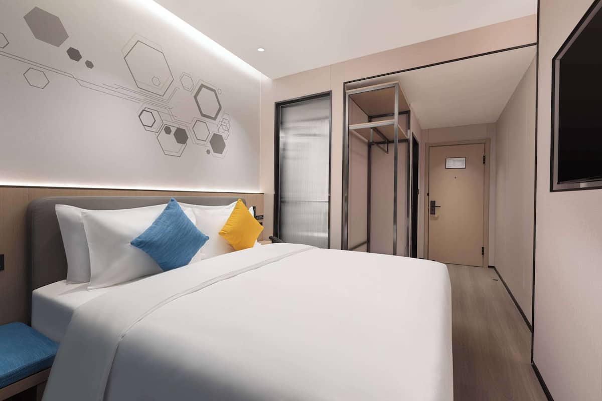 A modern hotel room with a large bed, a bedside table, and a wall with geometric patterns.