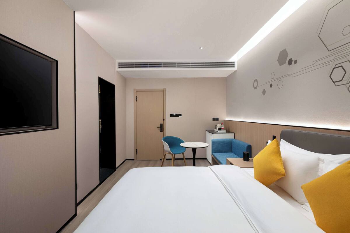 A modern hotel room with a large bed, a desk, a chair, and a TV mounted on the wall.