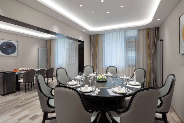 A modern dining area with a round table set for six, surrounded by chairs. There is a small bar area to the left with a counter and stools. The room has a large window with curtains, and the ceiling features recessed lighting. - Microtel By Wyndham Xian Beilin (Xi'an)