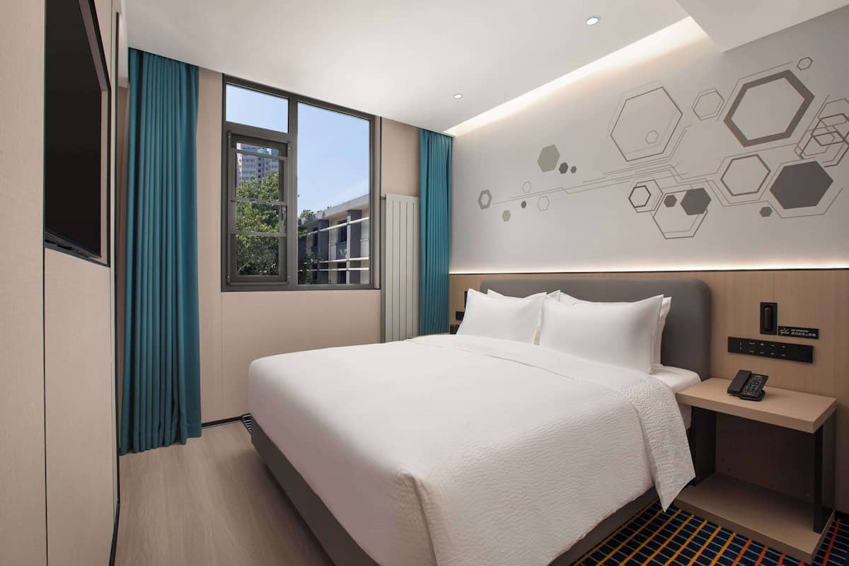 A modern hotel room with a large bed, a bedside table with a phone, and a wall with geometric patterns.