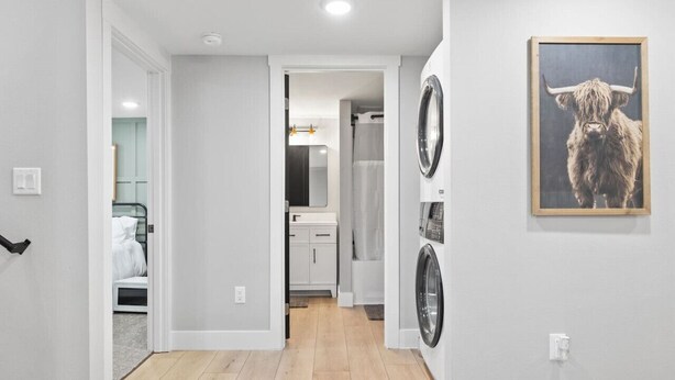 A hallway with a washing machine and dryer, a bed, and a bathroom visible through an open door. - Steps to Hospital and MSU-B| Renovated Hospital Retreat (Billings)