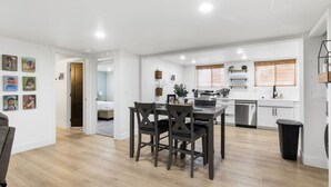 A modern kitchen with white cabinets, a stainless steel dishwasher, and a dining area with a dark wooden table and chairs.