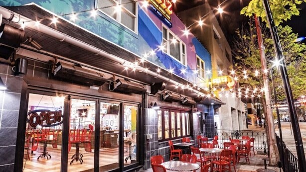 An outdoor seating area with red chairs and tables, a building with a 'SPITZ' sign, and string lights.