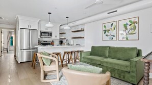 Eine moderne Küche mit weißen Schränken, einem Edelstahl-Kühlschrank und einer Mikrowelle. Im Wohnbereich befindet sich ein grünes Sofa und ein Couchtisch aus Holz.