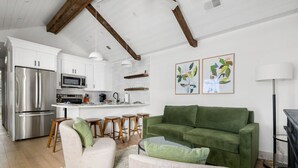 Una cocina moderna con armarios blancos, electrodomésticos de acero inoxidable y un sofá verde en una sala de estar.