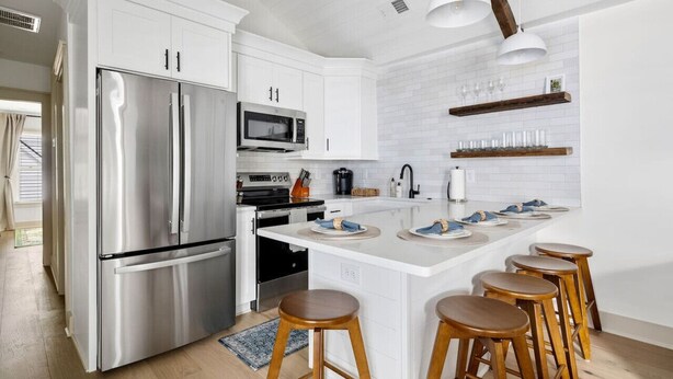 Una cocina moderna con armarios blancos, electrodomésticos de acero inoxidable y taburetes de madera.