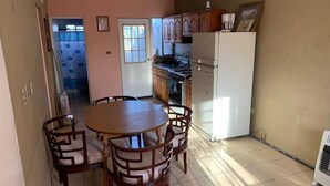 Un comedor con una mesa redonda de madera y sillas, una cocina con armarios y electrodomésticos de madera, y un piso con baldosas.