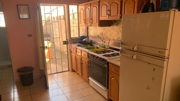 Una cocina con gabinetes de madera, estufa a gas, refrigerador y piso de baldosas.