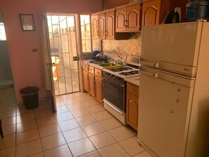 A kitchen with wooden cabinets, a gas stove, a refrigerator, and a tiled floor.