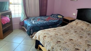 Un dormitorio con dos camas, una ventana con cortinas, un espejo y un estante con ropa doblada.