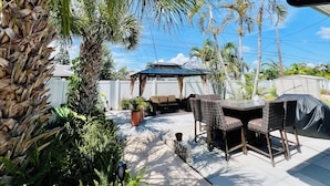 Un espace patio aménagé avec une table et des chaises, entouré de palmiers et de plantes.