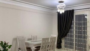 Un coin repas avec une table et des chaises blanches, une plante en pot et un sol carrelé.