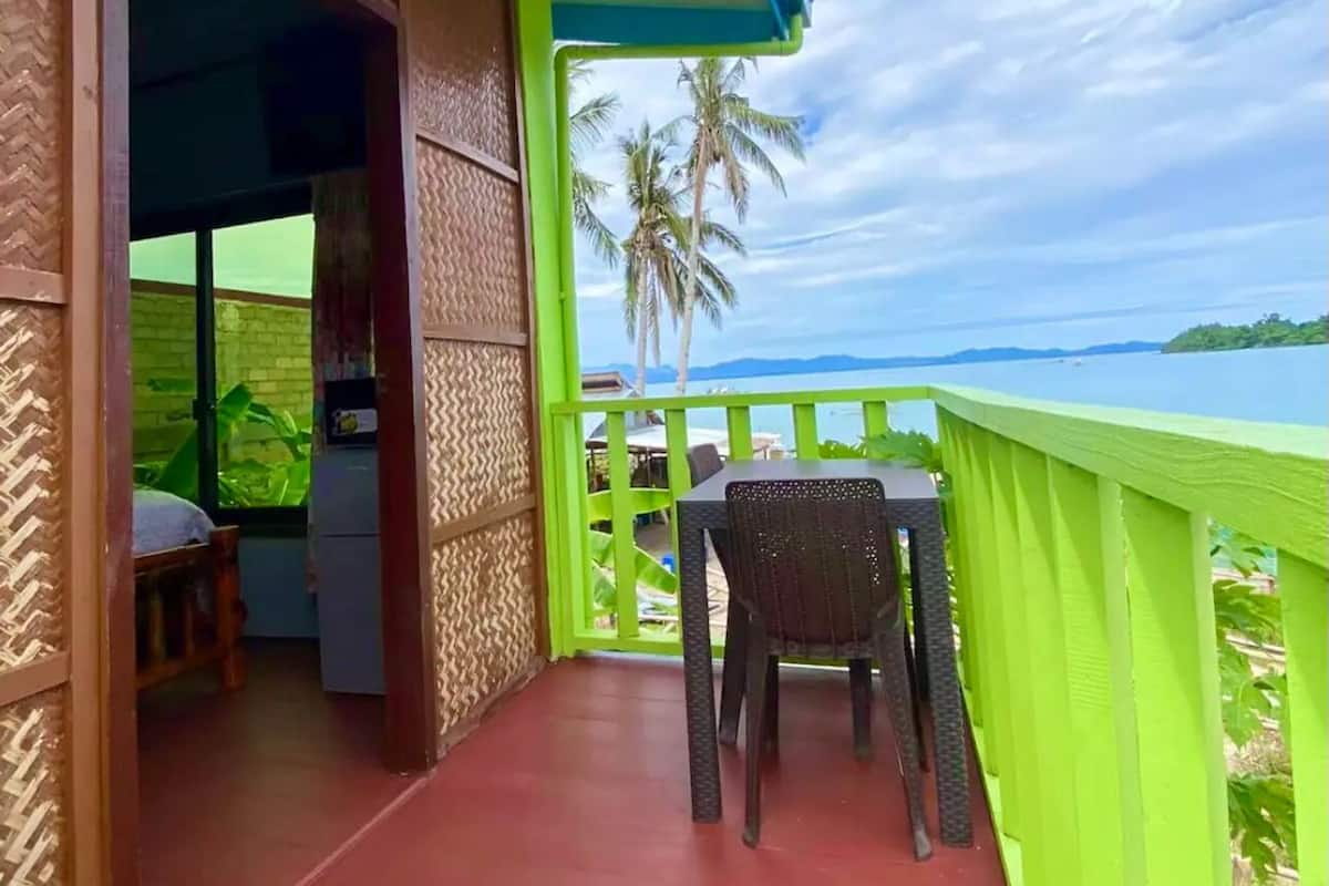 Un balcón con vistas al mar y palmeras, una mesa y una silla.