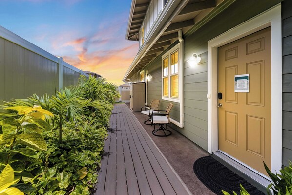 A wooden deck with chairs and a door, surrounded by greenery. - Studio Nene by AvantStay | Chic, Cozy, King Bed (Waianae)