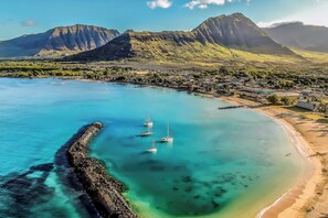 A coastal town with a clear blue bay, a rocky breakwater, and sailboats anchored near the shore. - Studio Nene by AvantStay | Chic, Cozy, King Bed (Waianae)