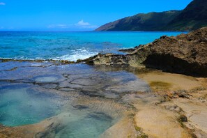A coastal landscape with clear waters, rocky terrain, and distant mountains. - Studio Nene by AvantStay | Chic, Cozy, King Bed (Waianae)
