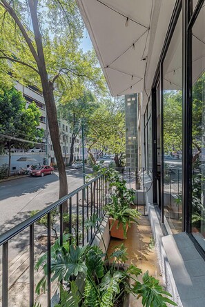 A balcony with potted plants, a view of the street, and a building with large windows. - Amalli Refugio Urbano (Mexico City)