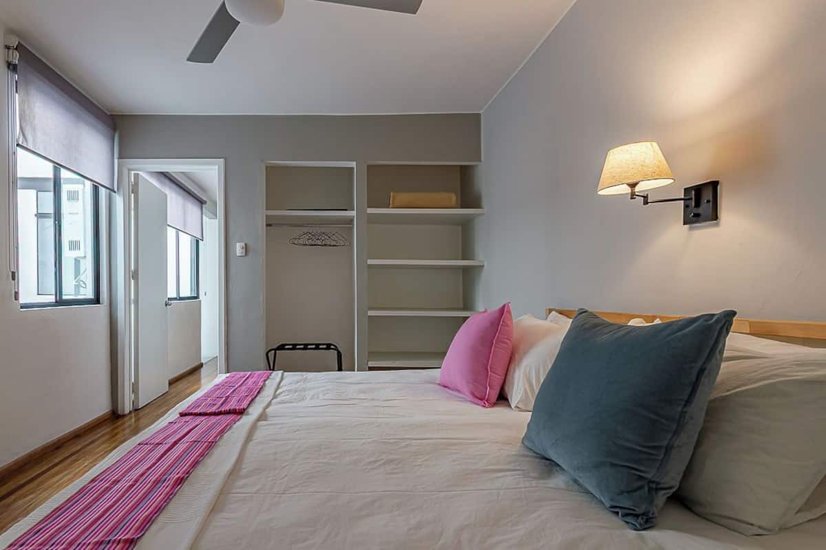 A bedroom with a bed, pillows, a bedside lamp, a wardrobe, and a window.