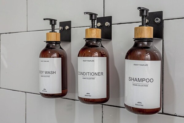 Three bottles of body wash, conditioner, and shampoo hanging on a tiled wall. - Amalli Refugio Urbano (Mexico City)