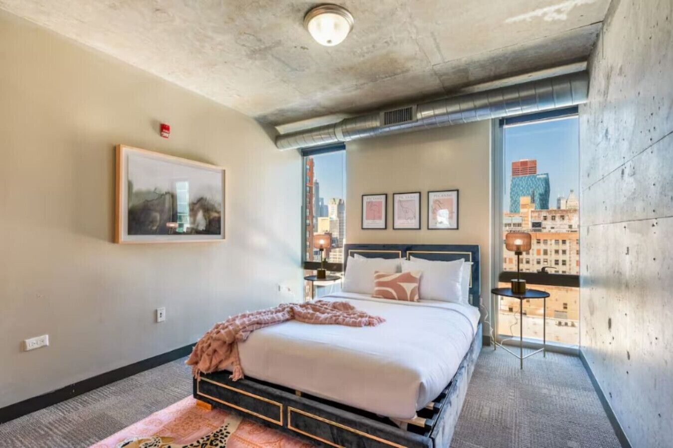 Une chambre d’hôtel moderne avec un grand lit, une vue sur la ville et un tableau encadré au mur.