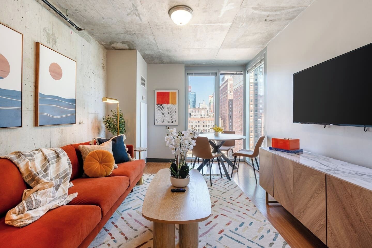 A modern living room with a red sofa, a dining table, and a kitchen area with a marble countertop.
