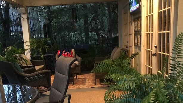 An outdoor seating area with a round table and chairs, surrounded by potted plants and a large fern.
