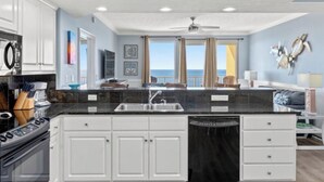 A modern kitchen with white cabinets, a black countertop, and a dishwasher. There is a large window with a view of the ocean. - Beachfront PCB Rentals 1406: large balcony, owner managed, Free Beach Service! (Panama City Beach)