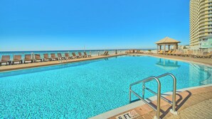 A swimming pool with lounge chairs and a gazebo, surrounded by a high-rise building. - Beachfront PCB Rentals 1406: large balcony, owner managed, Free Beach Service! (Panama City Beach)