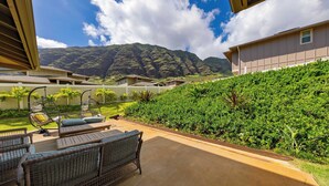 Eine Terrasse mit Gartenmöbeln, Blick auf einen Berg und einen gepflegten Garten.