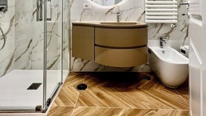 A modern bathroom with a glass shower enclosure, a marble-tiled wall, a wooden floor, a round mirror, a sink with a vanity, and a bidet. - IDEAL SUITE 41 - SALERNO AMALFI COAST POMPEI NAPLES PAESTUM (Pagani)