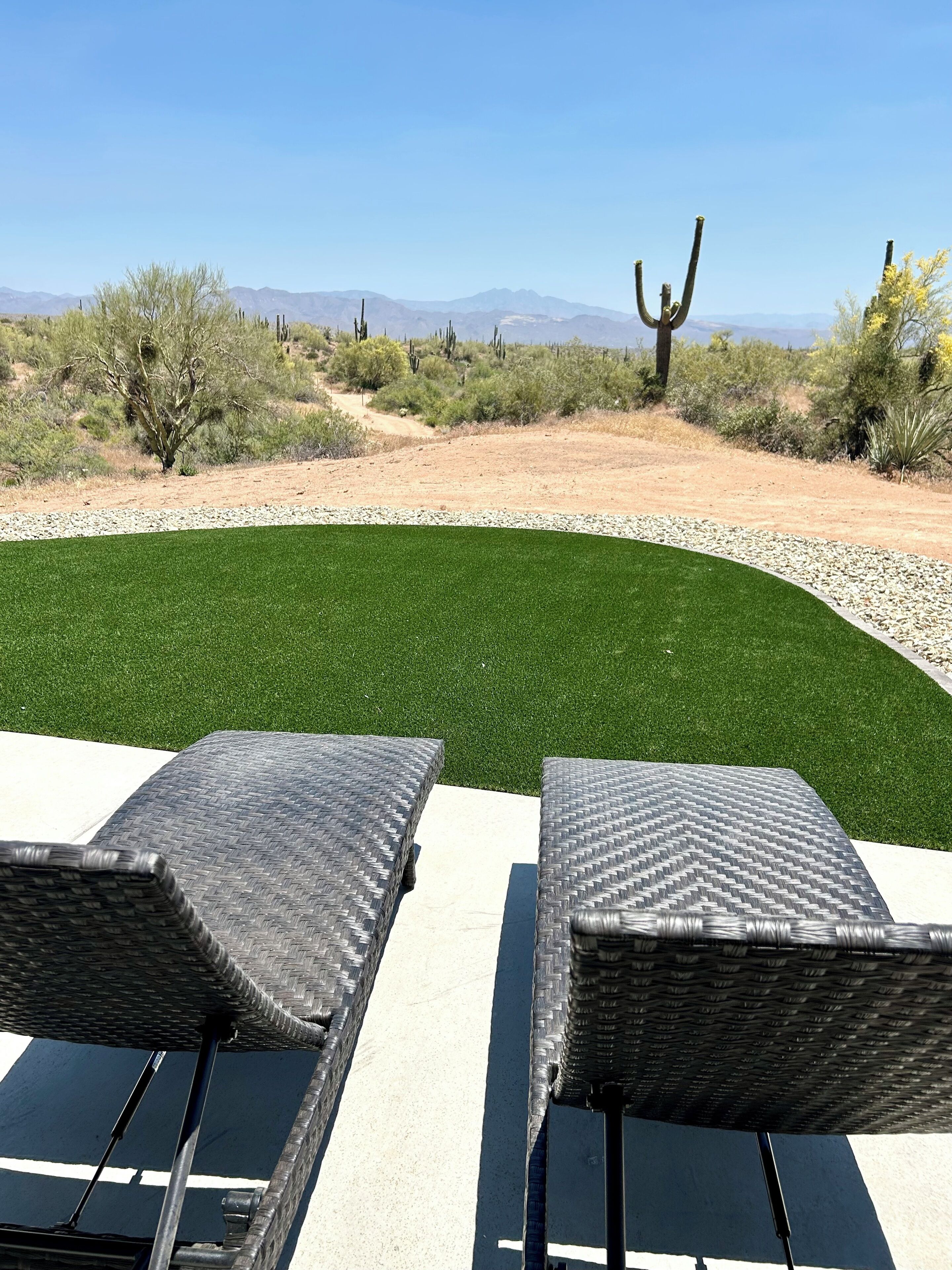 Deux fauteuils de jardin en osier, placés face à une pelouse verdoyante, avec un paysage désertique en arrière-plan.