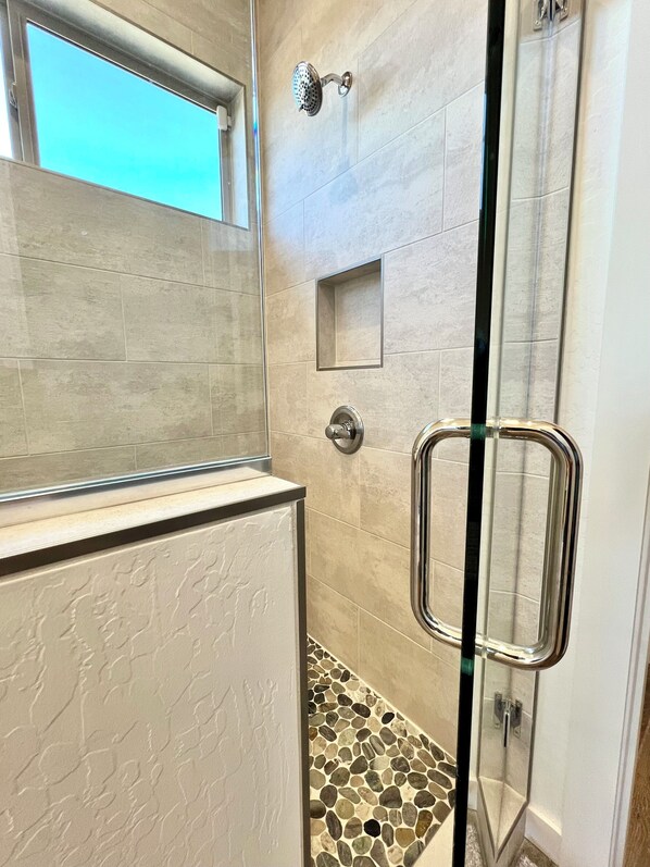 Ein modernes Badezimmer mit Duschkabine aus Glas, einem kleinen Fenster und einem gefliesten Boden.