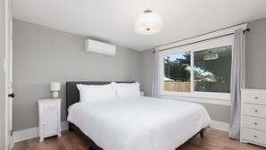 Un dormitorio con cama, mesita de noche, lámpara, equipo de aire acondicionado y ventana con cortinas.