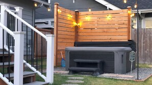Un patio trasero con jacuzzi, terraza de madera y una escalera que lleva a una casa.