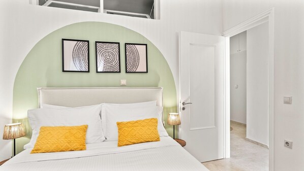 Un dormitorio con una cama blanca, dos almohadas amarillas, un cabecero blanco y tres obras de arte enmarcadas sobre la cama.