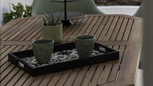Una mesa de madera con una bandeja que sostiene dos tazas y una planta en maceta.