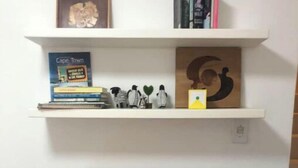 A study area with a wooden desk and chair, a bookshelf with books and decorative items, and a wall-mounted shelf above. - Havenzicht: sleep to the sound of the sea

 (Cape Town)