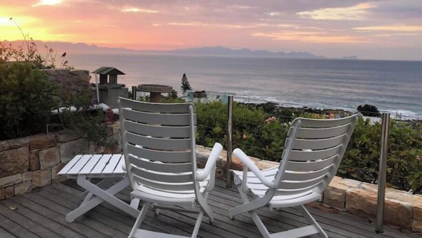 Two white lounge chairs on a wooden deck overlooking a coastal view with mountains in the distance. - Havenzicht: sleep to the sound of the sea

 (Cape Town)