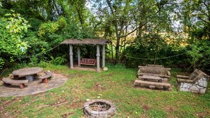 A rustic outdoor setting with a wooden bench, a stone fire pit, and a gazebo.