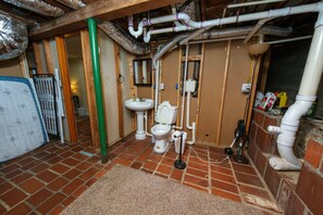 Une salle de bain avec des toilettes, un lavabo et des tuyaux apparents.
