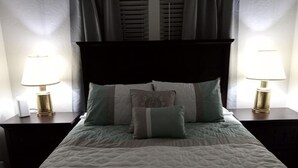 A neatly made bed with a patterned bedspread, two bedside lamps, and a dark headboard.