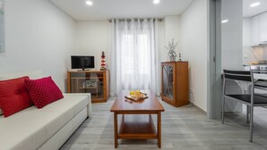 A modern living room with a sofa, a wooden coffee table, a television, and a kitchen area visible through an open door. - Casa da Areia - 3 minutes from the beach (Nazaré)