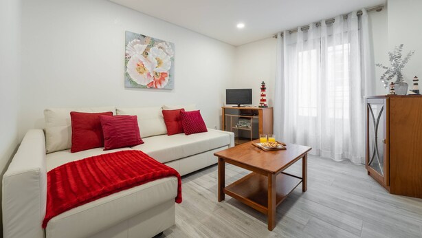A modern living room with a white sofa, red cushions, a wooden coffee table, and a painting on the wall. - Casa da Areia - 3 minutes from the beach (Nazaré)