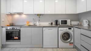A modern kitchen with white cabinets, a built-in oven, a dishwasher, and a washing machine. - Casa da Areia - 3 minutes from the beach (Nazaré)