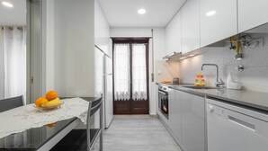 A modern kitchen with a dining area, featuring a glass table with a fruit bowl, a built-in oven, and a dishwasher. - Casa da Areia - 3 minutes from the beach (Nazaré)