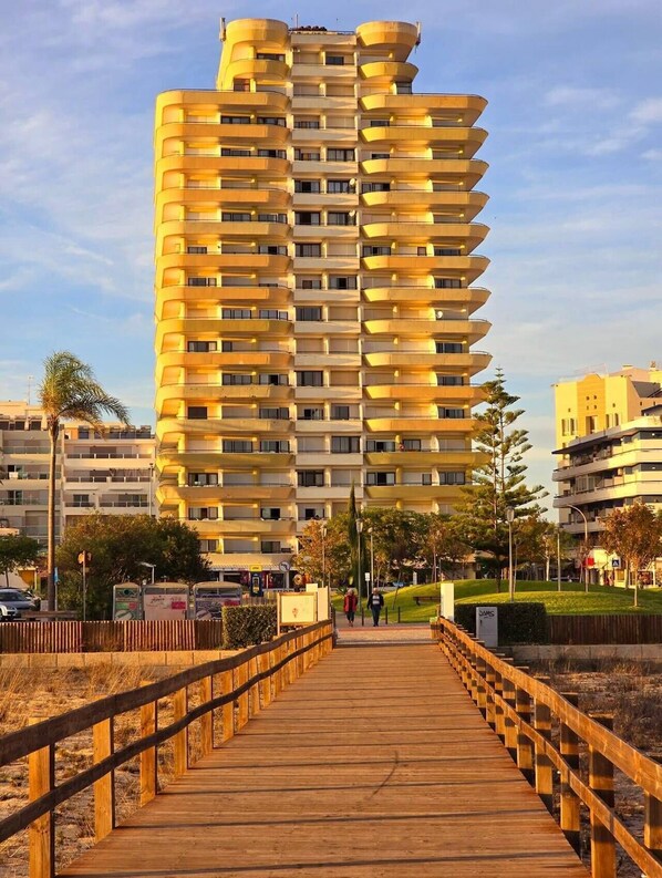 A multi-story building with balconies, a wooden boardwalk in front, and a clear sky.