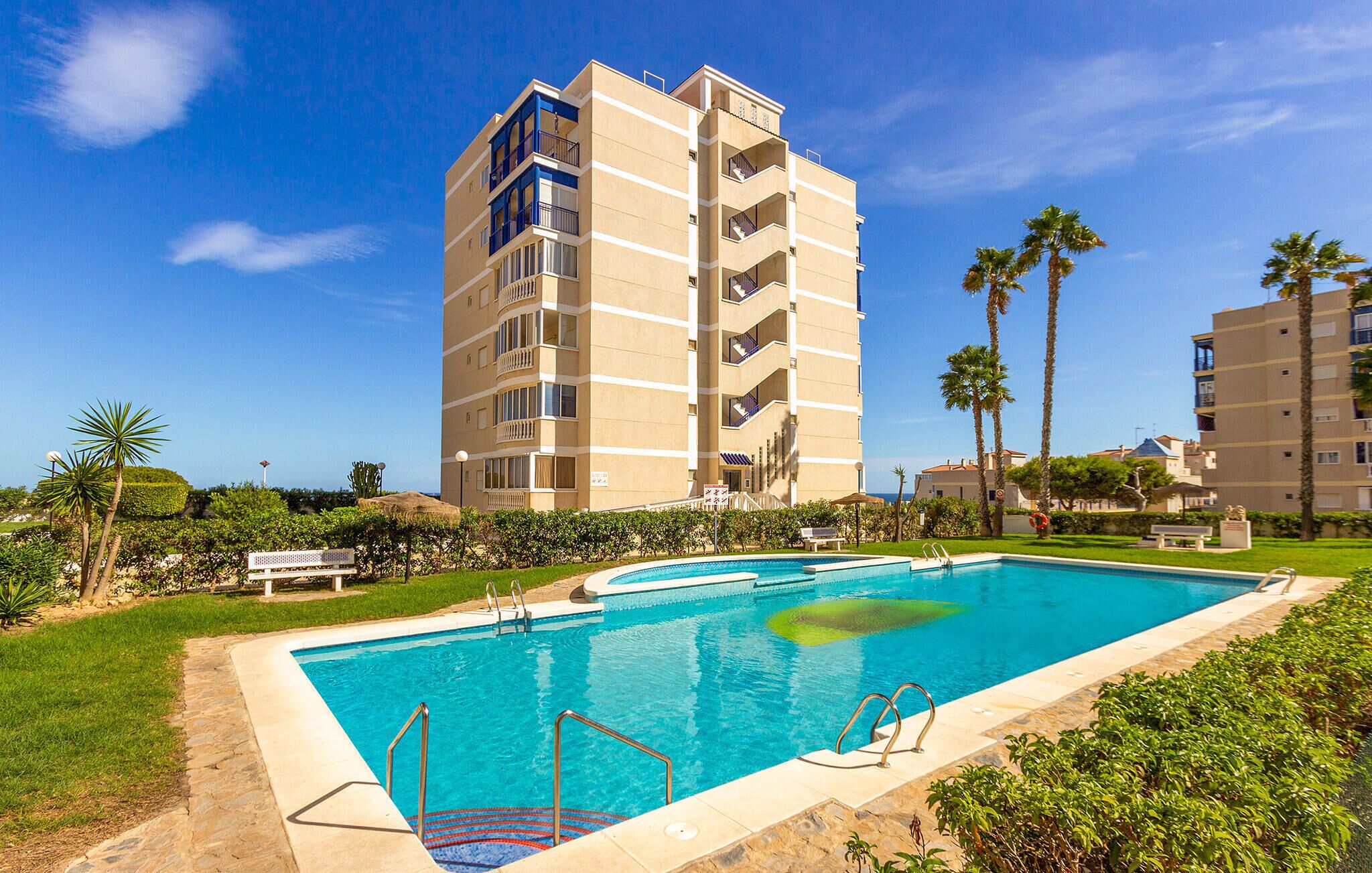 Un hôtel doté d’une piscine, entouré de palmiers et surplombant un ciel d’un bleu limpide.
