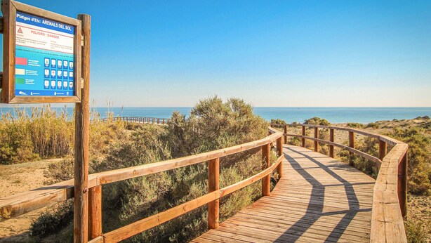 Une promenade en bois menant à une plage, avec un panneau d’avertissement.