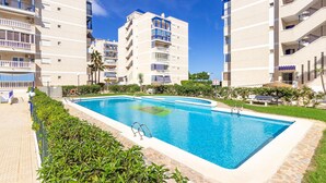 Une piscine entourée d’immeubles d’appartements dotés de balcons, un ciel dégagé et quelques espaces verts.